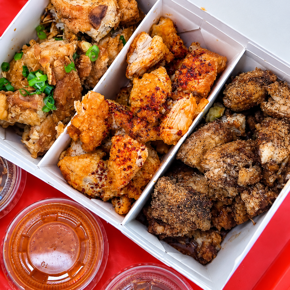 Three-compartment box of crispy seasoned chicken over rice with green onions, served with two dipping sauces on a red tray.