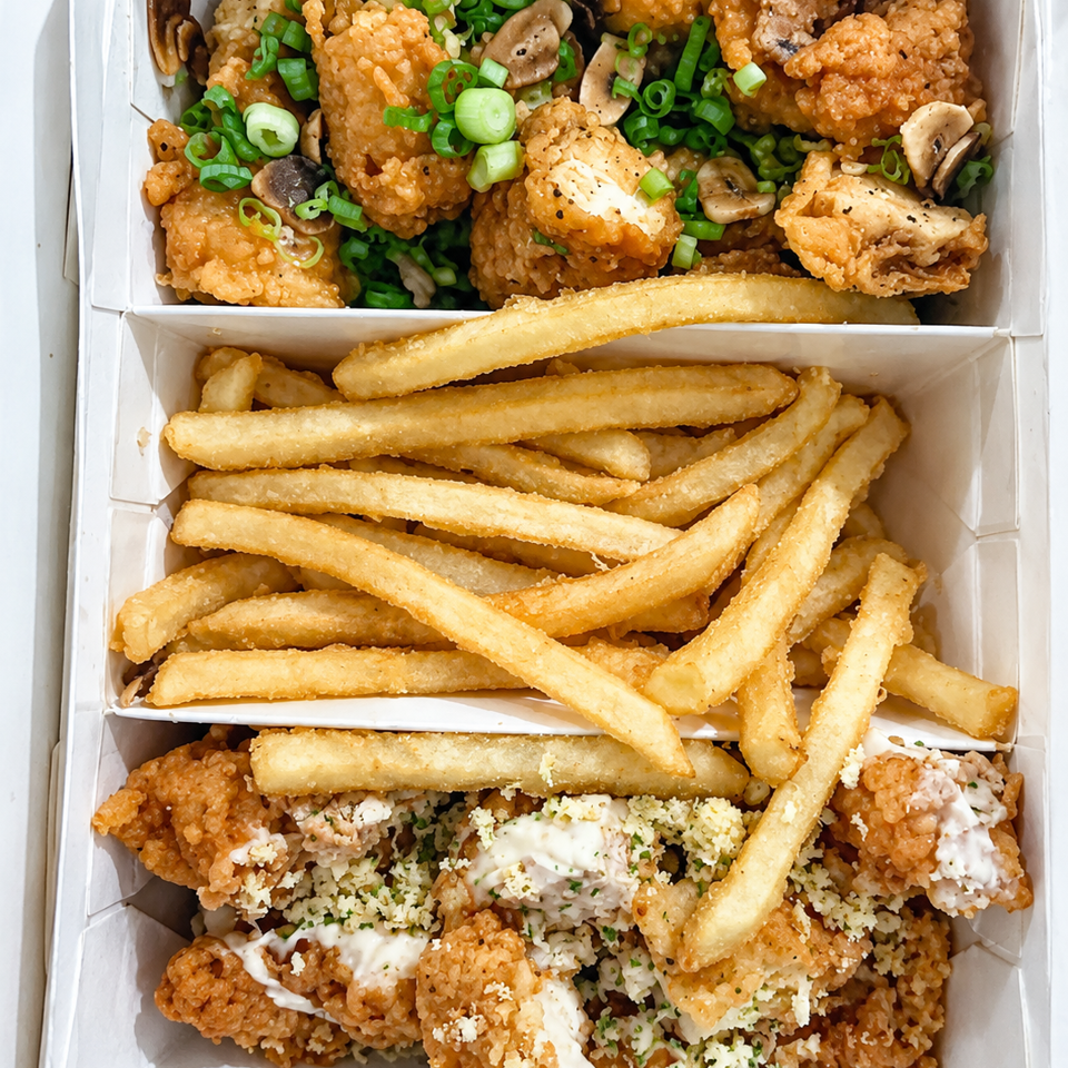 Open takeout box filled with crispy fried chicken, fries, mushrooms, green onions, creamy sauce, and grated cheese.